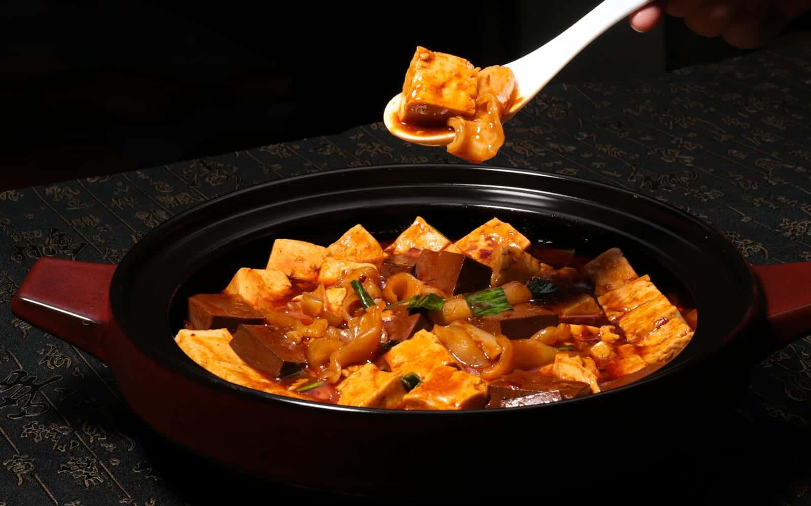 Mapo tofu with cubes of tofu in spicy red sauce in a black pot