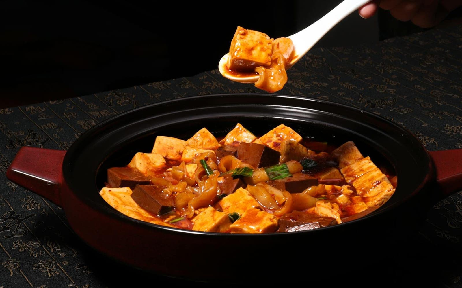 Mapo tofu with cubes of tofu in spicy red sauce in a black pot
