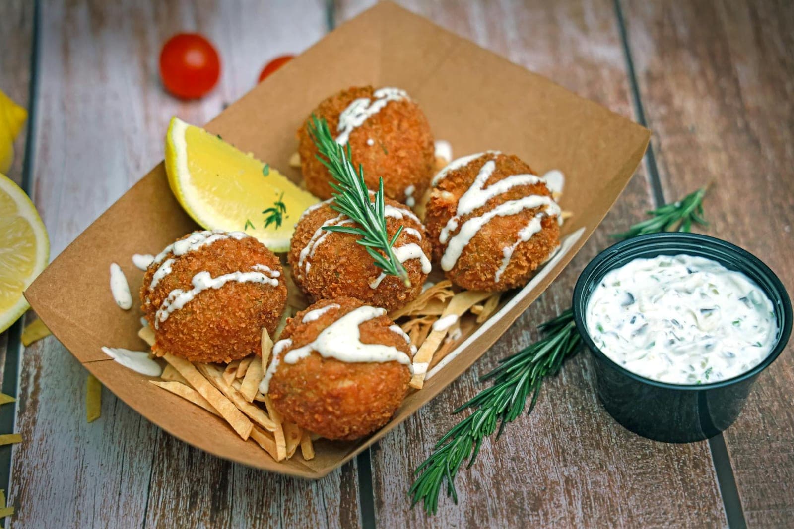 Maryland crab cakes with tartar sauce, lemon wedges, herbs, and fries in a paper tray