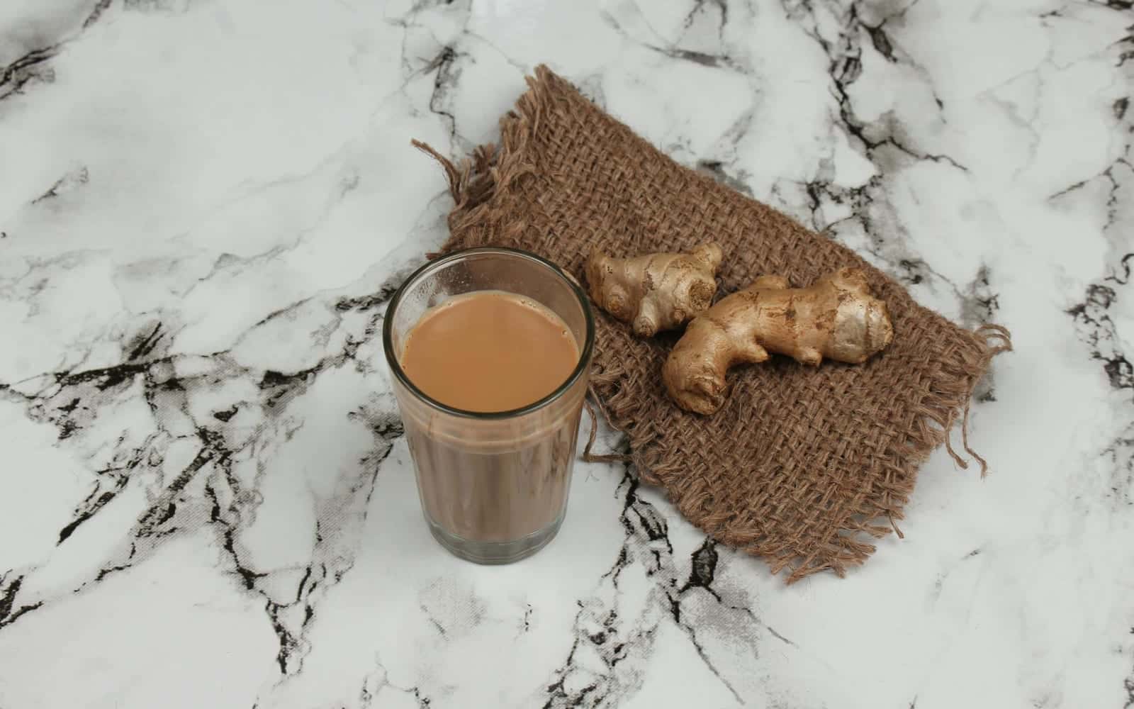 Masala chai in a glass with ginger on a marble surface