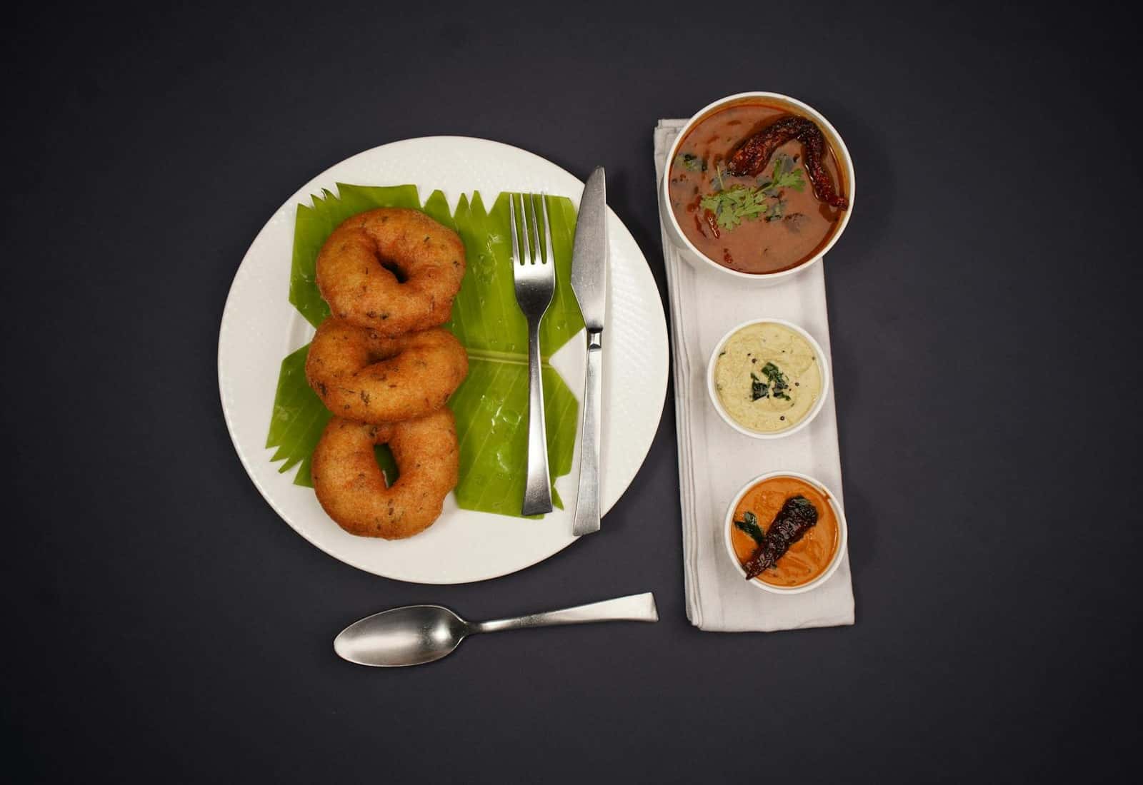 Medu vada South Indian fried lentil doughnuts served with chutneys and sambar on a black background
