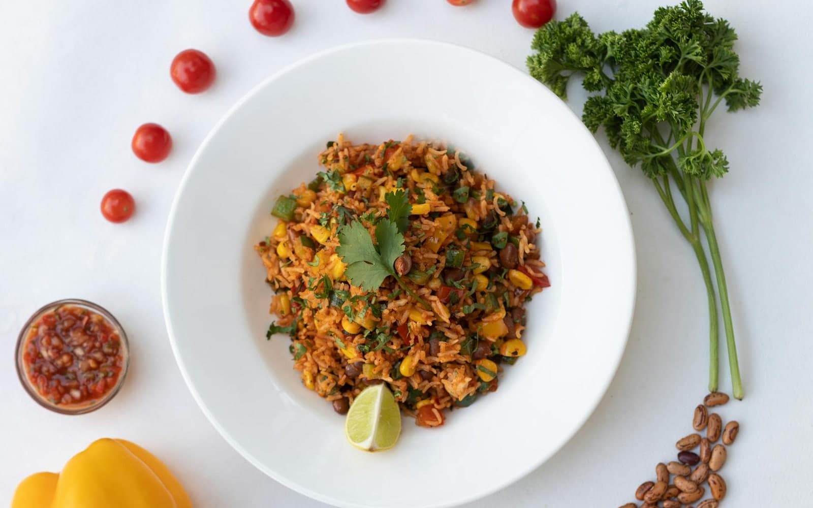 Mexican rice with vegetables, lime, herbs, and salsa on a white plate