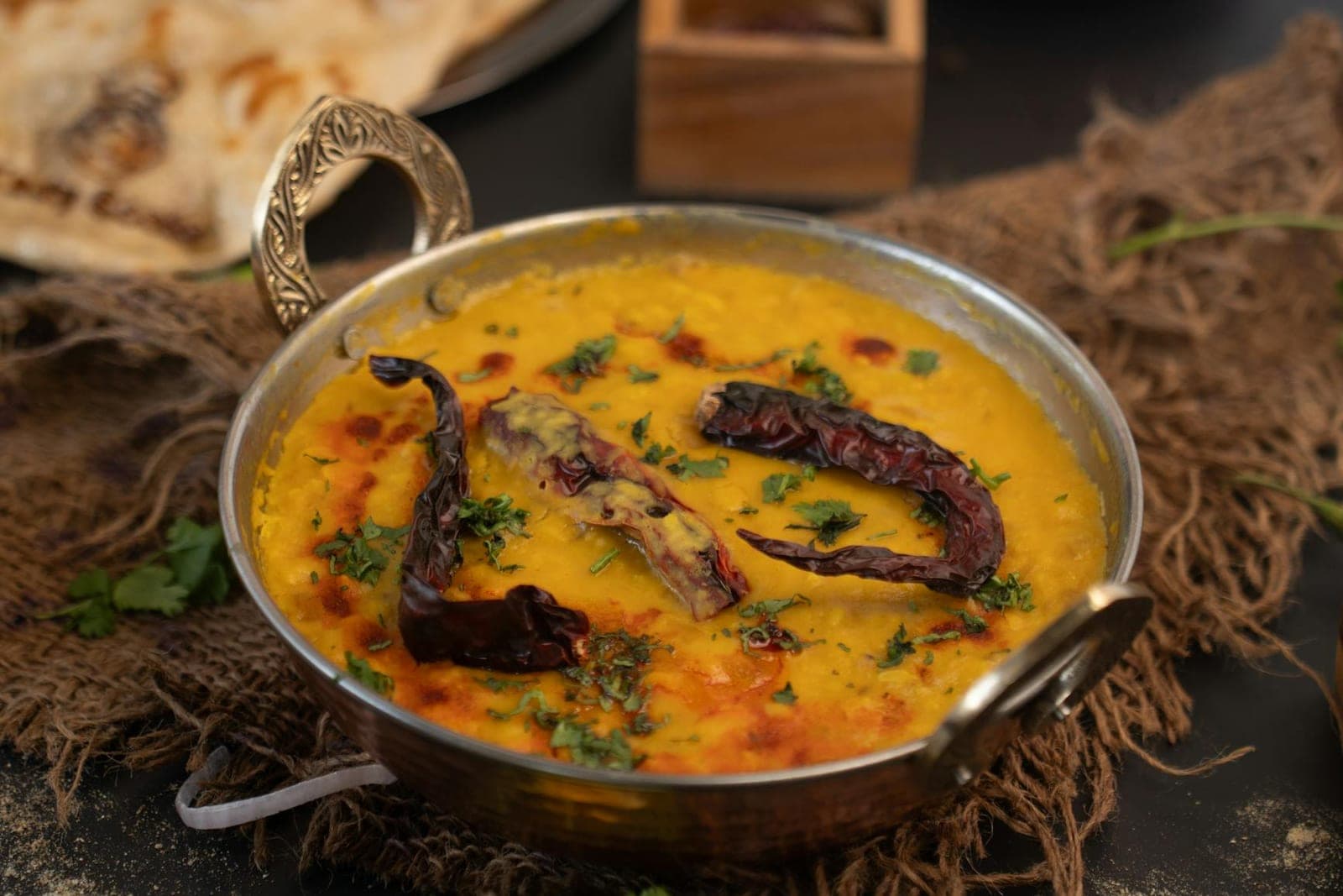 Moong dal yellow lentil curry in a metal serving bowl with dried chilies and herbs