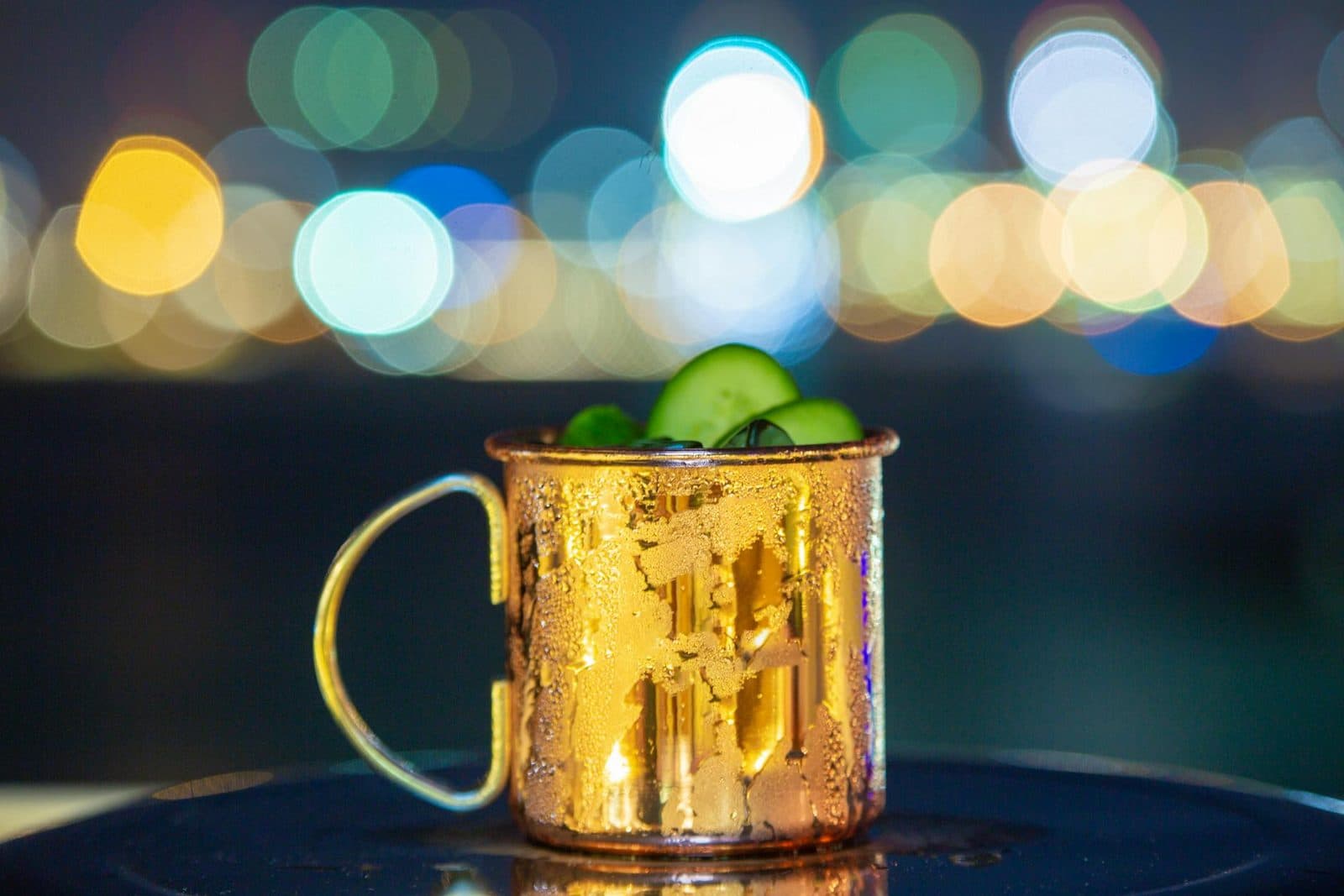 Moscow mule cocktail in a copper mug with lime and mint against city lights