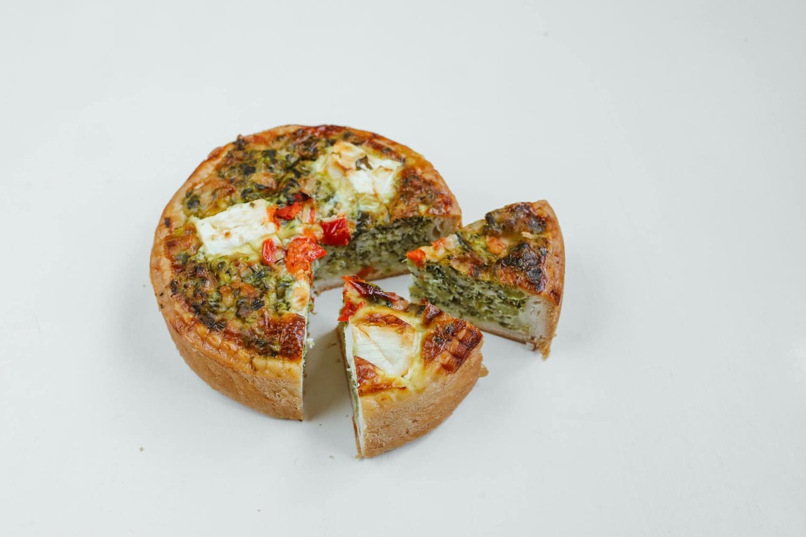Mushroom and spinach quiche with a sliced wedge, tomatoes, and herbs on a white background