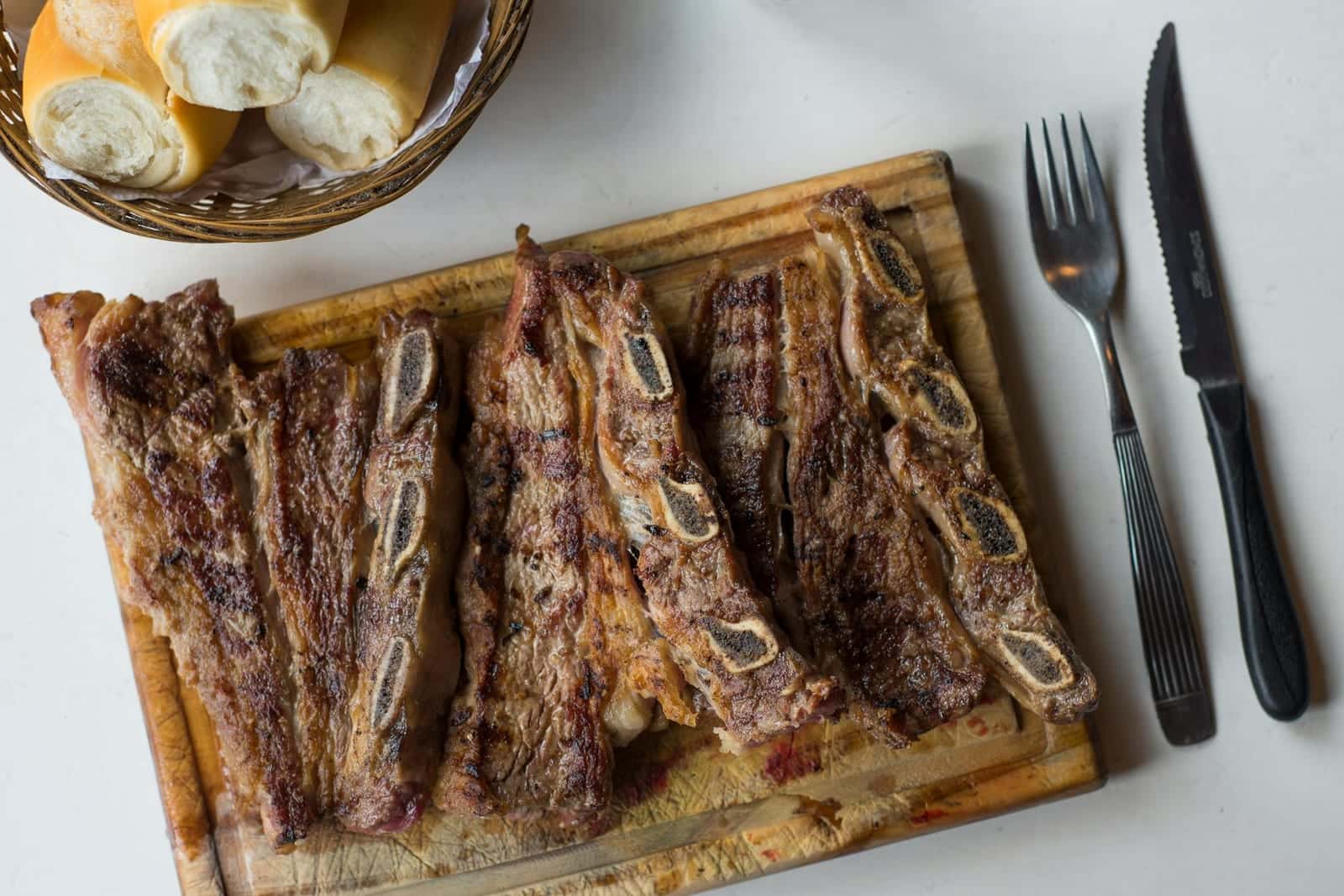 Oven-baked beef ribs served on a wooden board with bread and a simple table setting