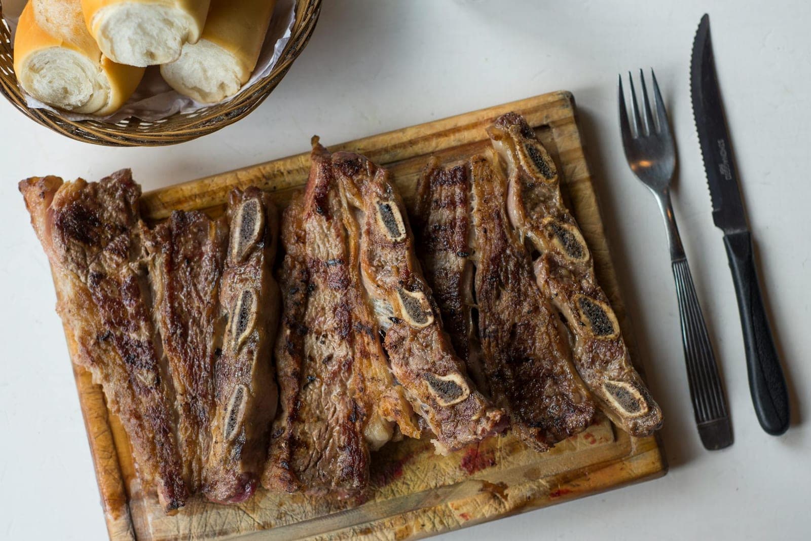 Oven-baked beef ribs served on a wooden board with bread and a simple table setting