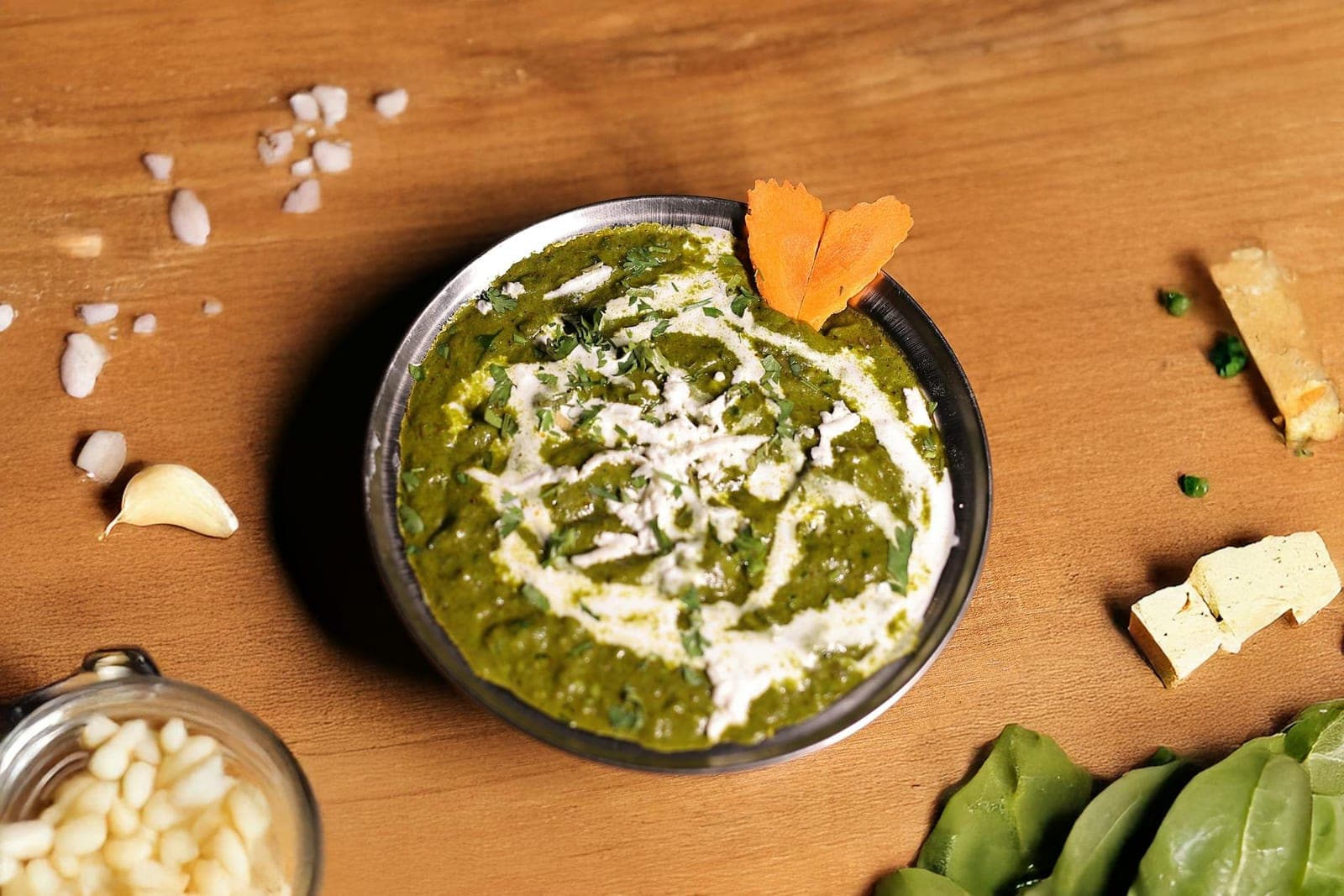 Palak paneer spinach curry garnished with cream and paneer pieces on a wooden board