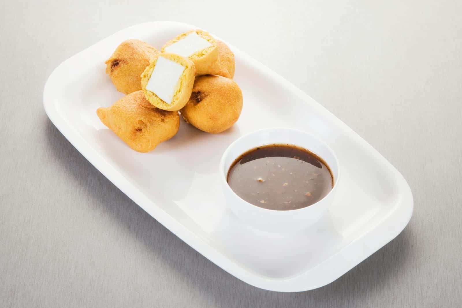 Paneer pakora fried Indian snack pieces served with chutney on a white plate