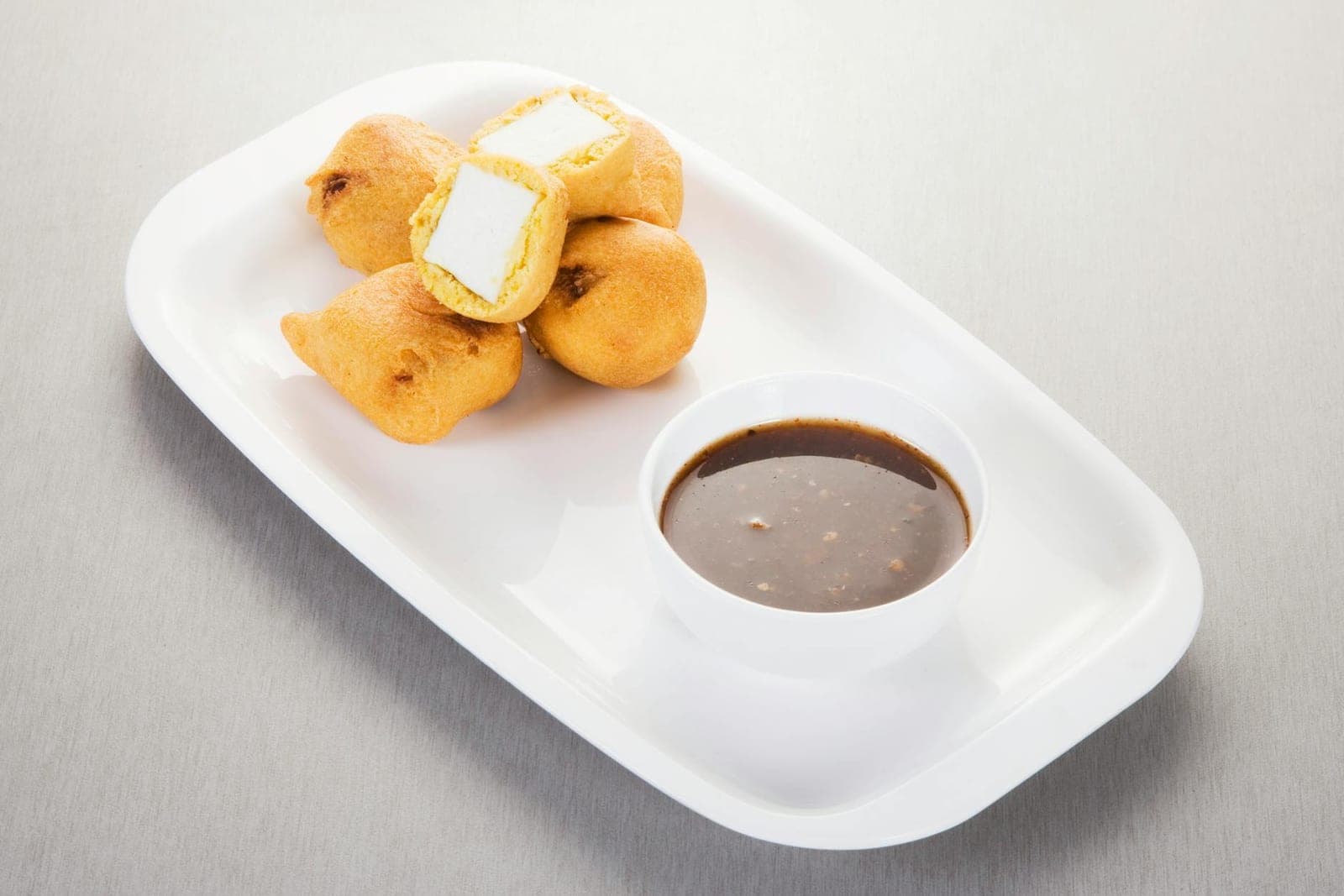 Paneer pakora fried Indian snack pieces served with chutney on a white plate