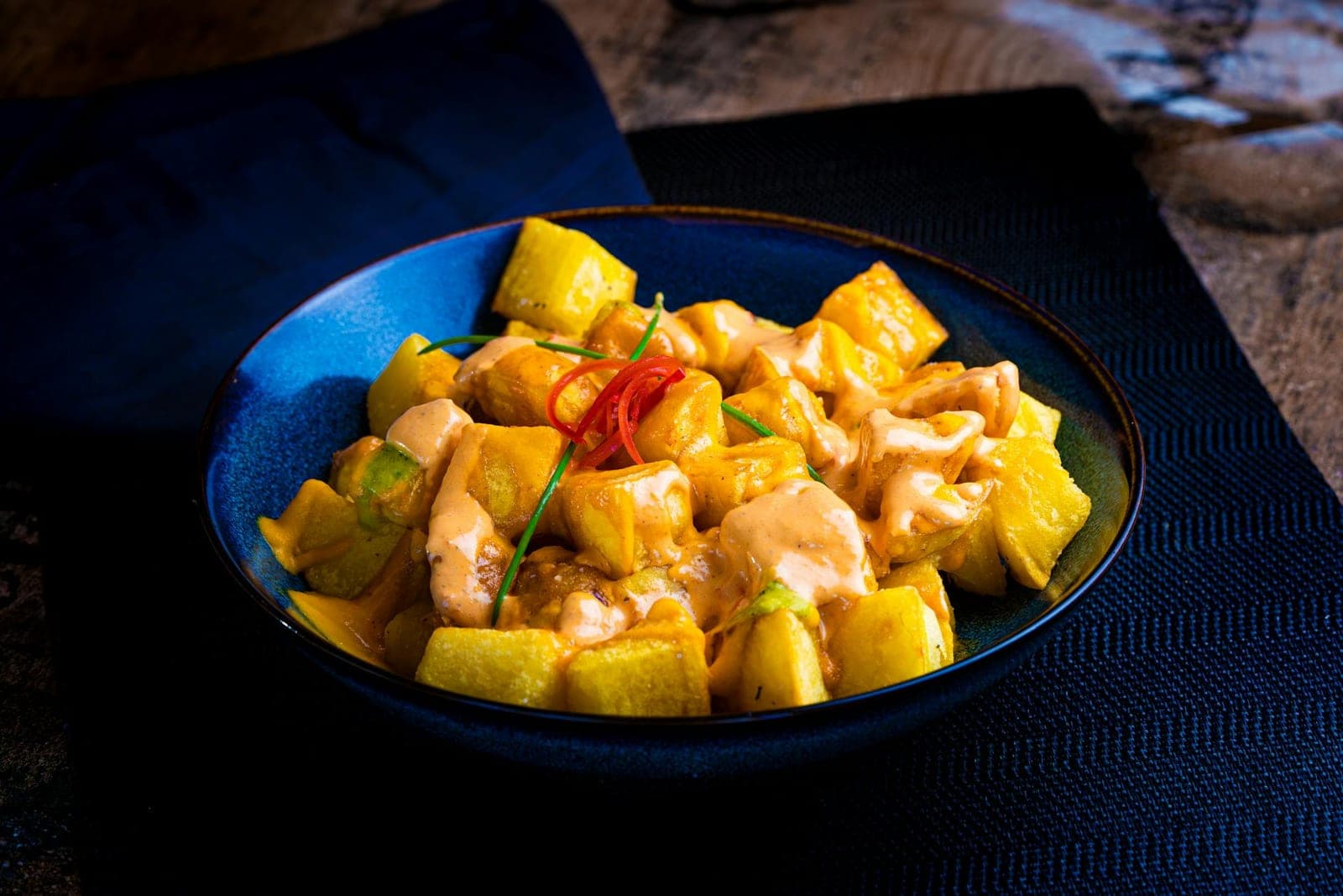 Patatas bravas potatoes with golden edges and red sauce in a dark bowl