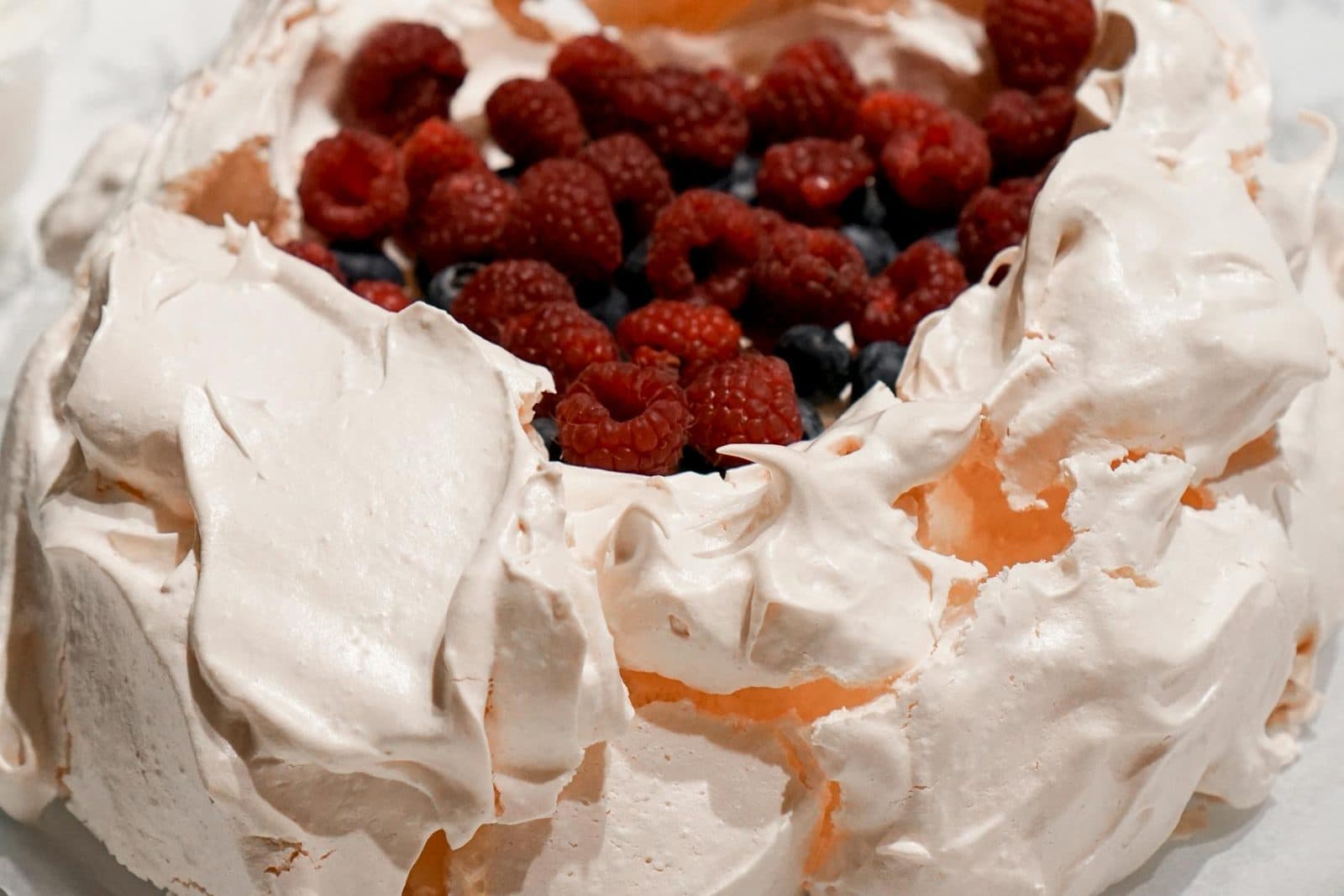 Pavlova with crisp meringue, whipped cream, raspberries, blueberries, and pomegranate