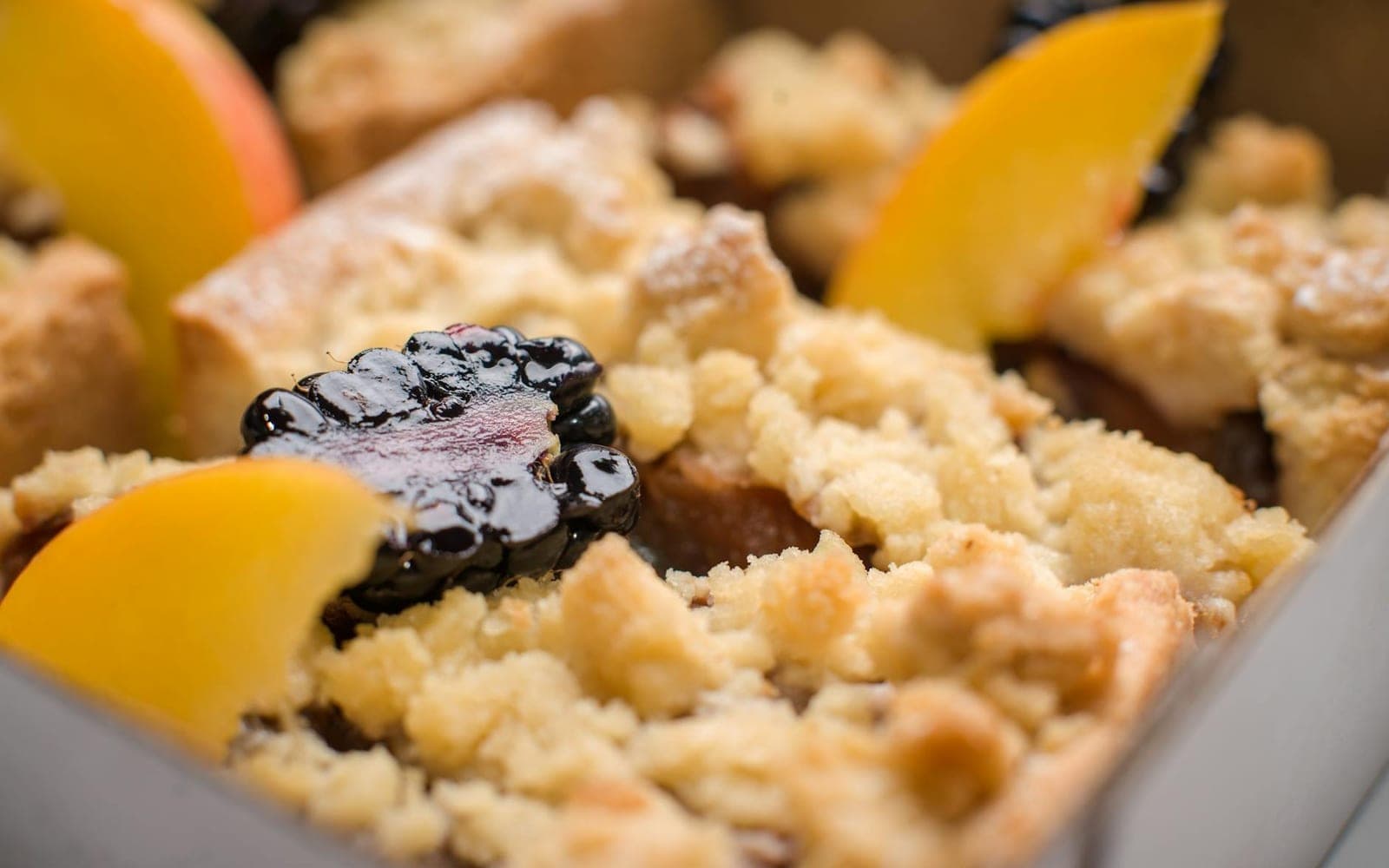 Peach cobbler with golden crumble topping, peach slices, and berries