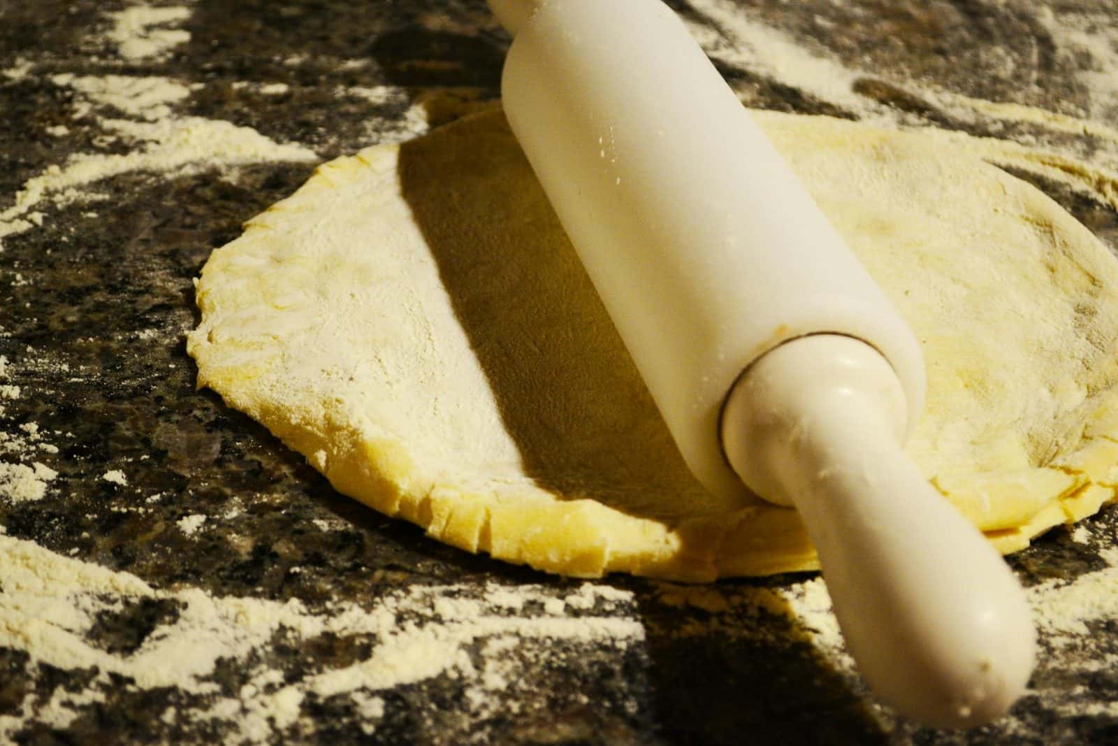 Pie crust dough being rolled on a floured work surface with a wooden rolling pin