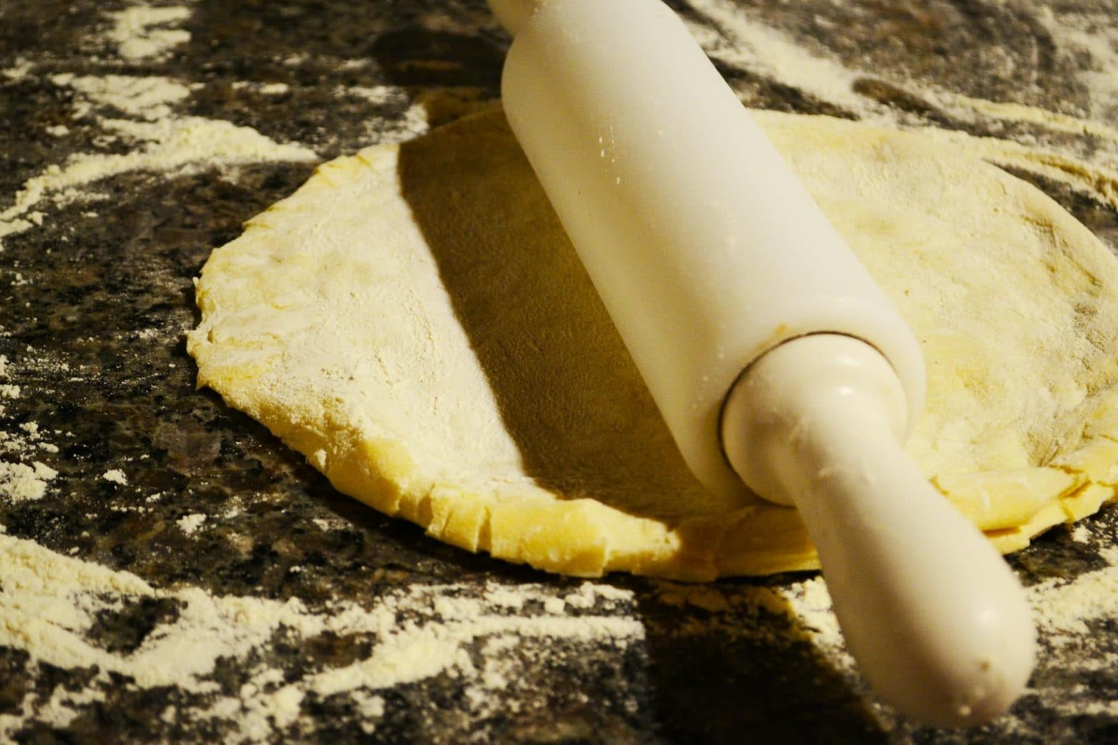 Pie crust dough being rolled on a floured work surface with a wooden rolling pin