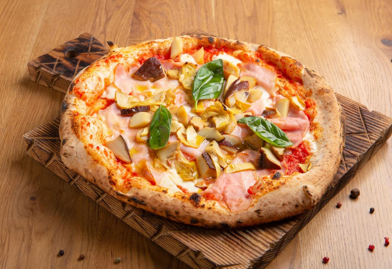 Pizza Capricciosa with artichoke, mushrooms, ham, tomato sauce, and basil on a wooden board
