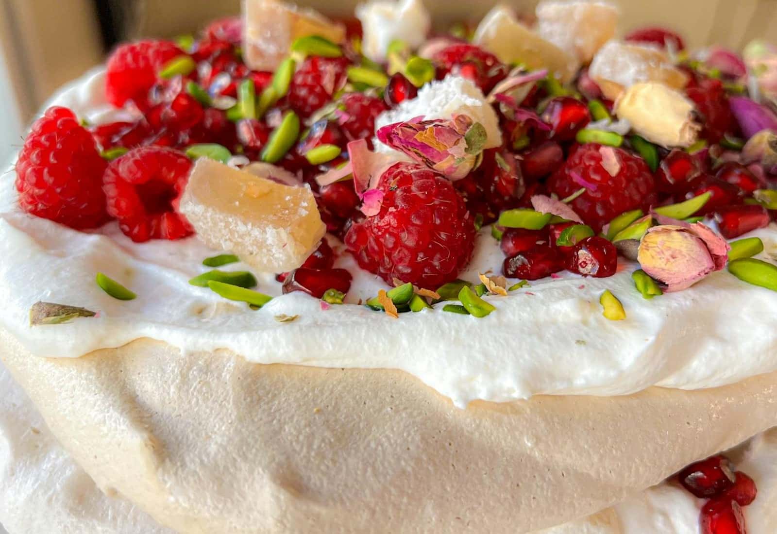 Raspberry pavlova with meringue, cream, raspberries, pistachios, and pomegranate on top