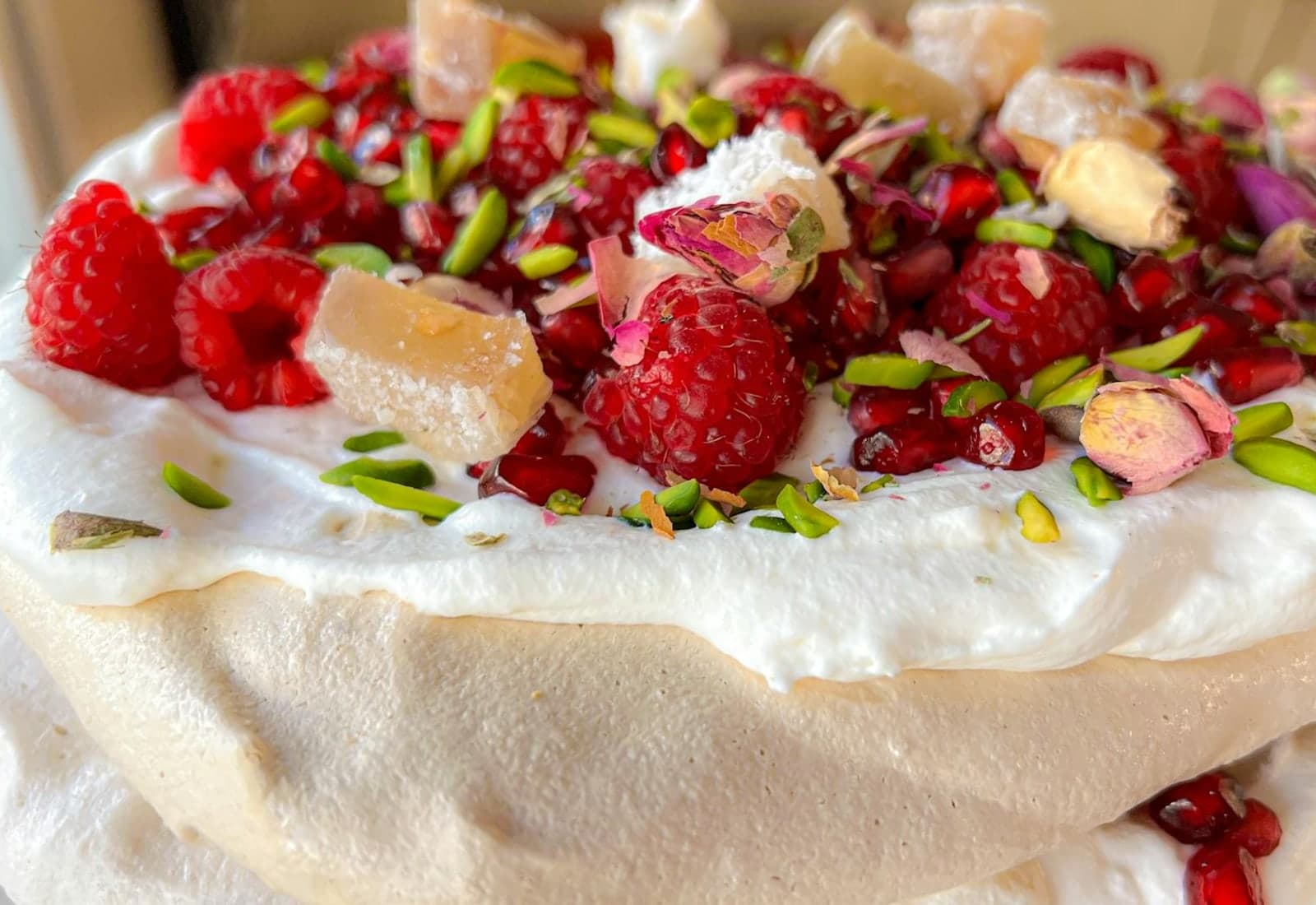 Raspberry pavlova with meringue, cream, raspberries, pistachios, and pomegranate on top