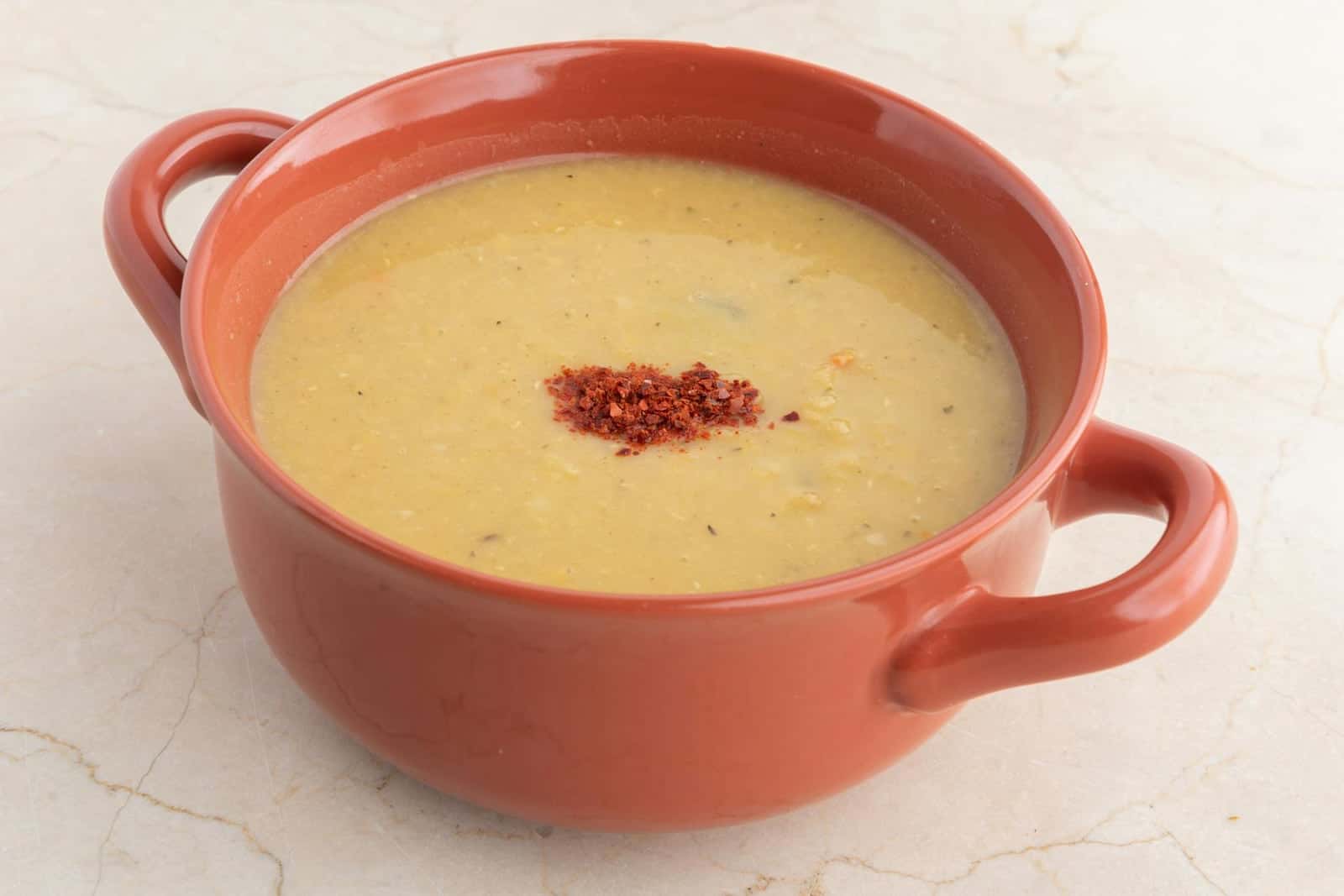 Red lentil soup in a terracotta handled bowl with paprika garnish