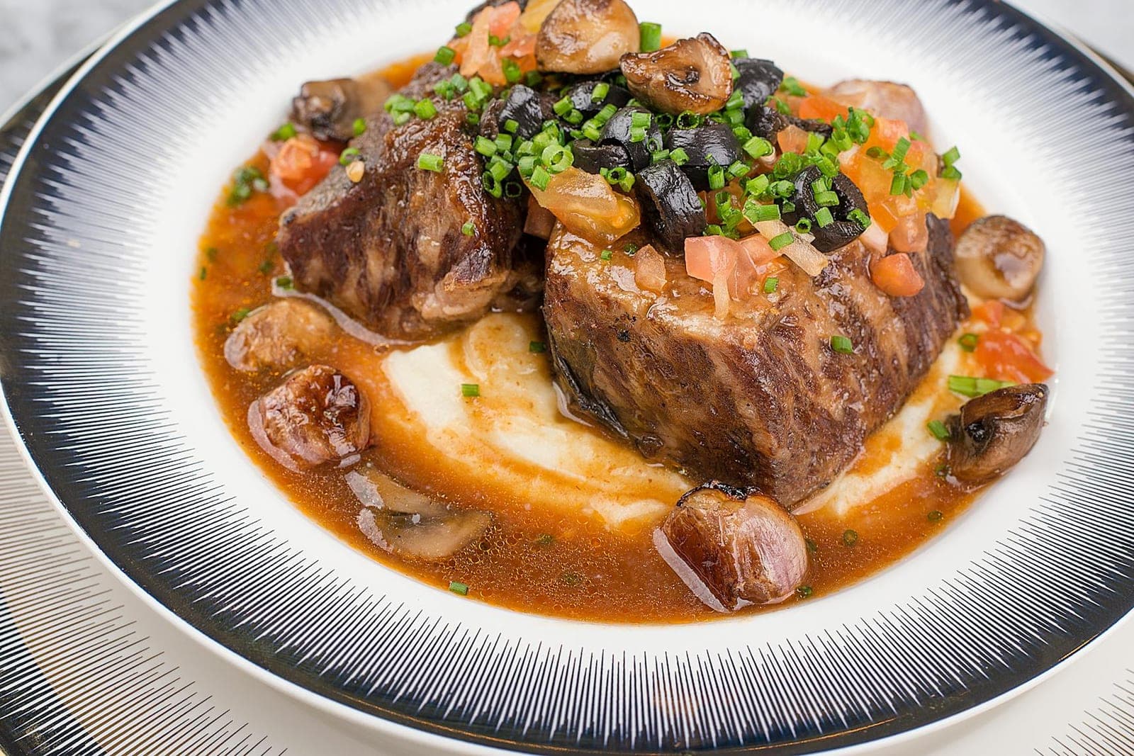 Red wine braised short ribs with mushrooms, chives, sauce, and mashed potatoes on a white plate