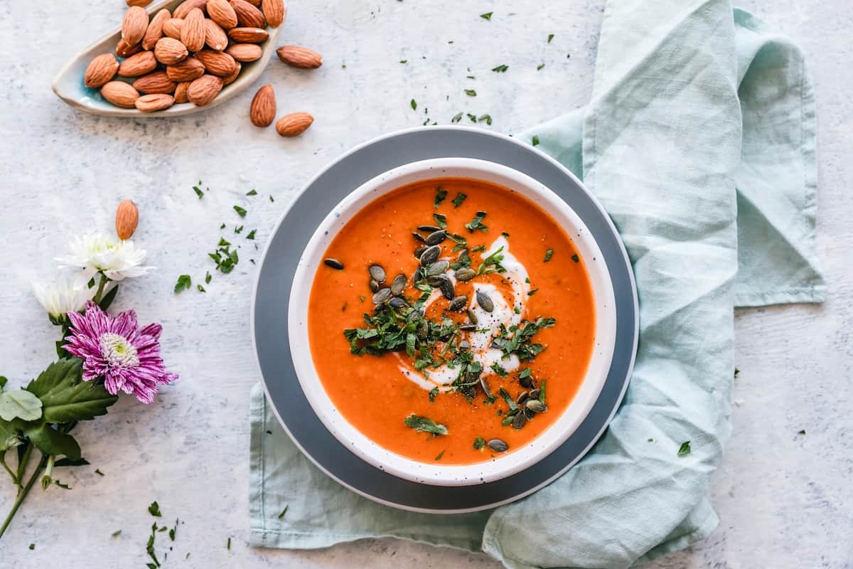 Bowl of smooth orange roasted vegetable soup garnished with herbs