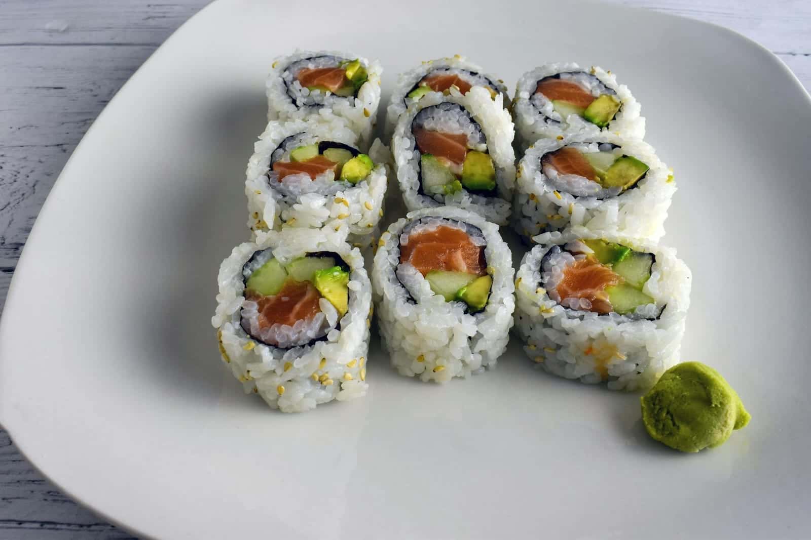 Salmon and avocado sushi rolls on a white plate with wasabi on the side