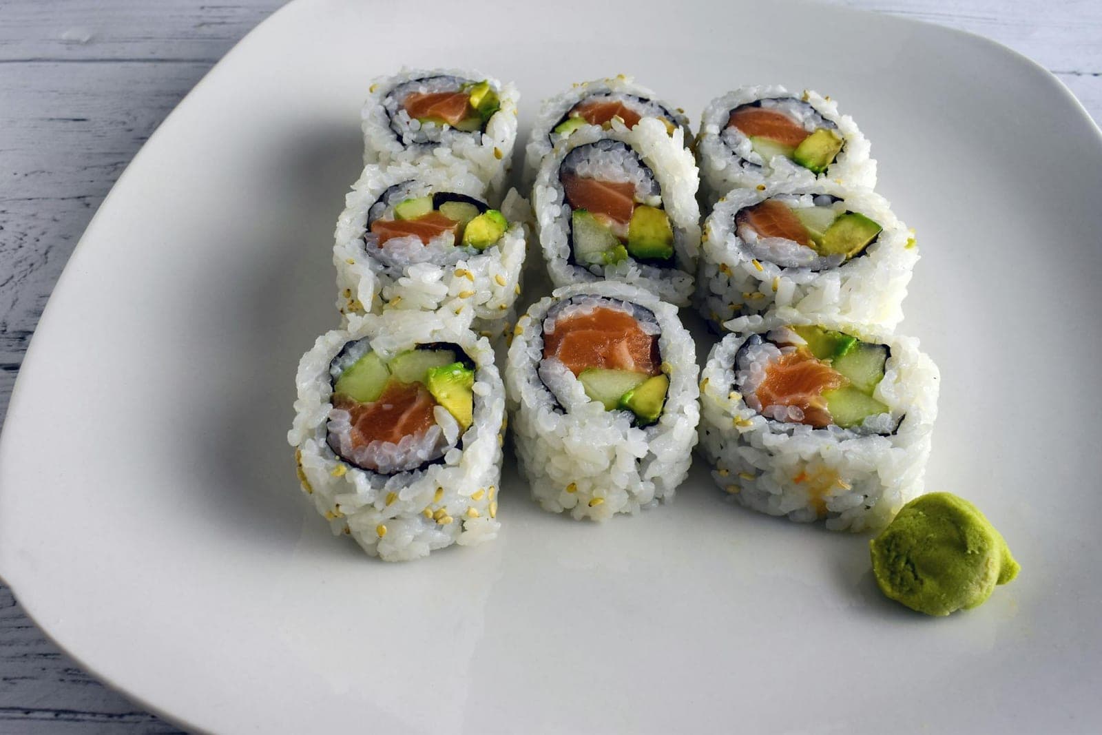 Salmon and avocado sushi rolls on a white plate with wasabi on the side