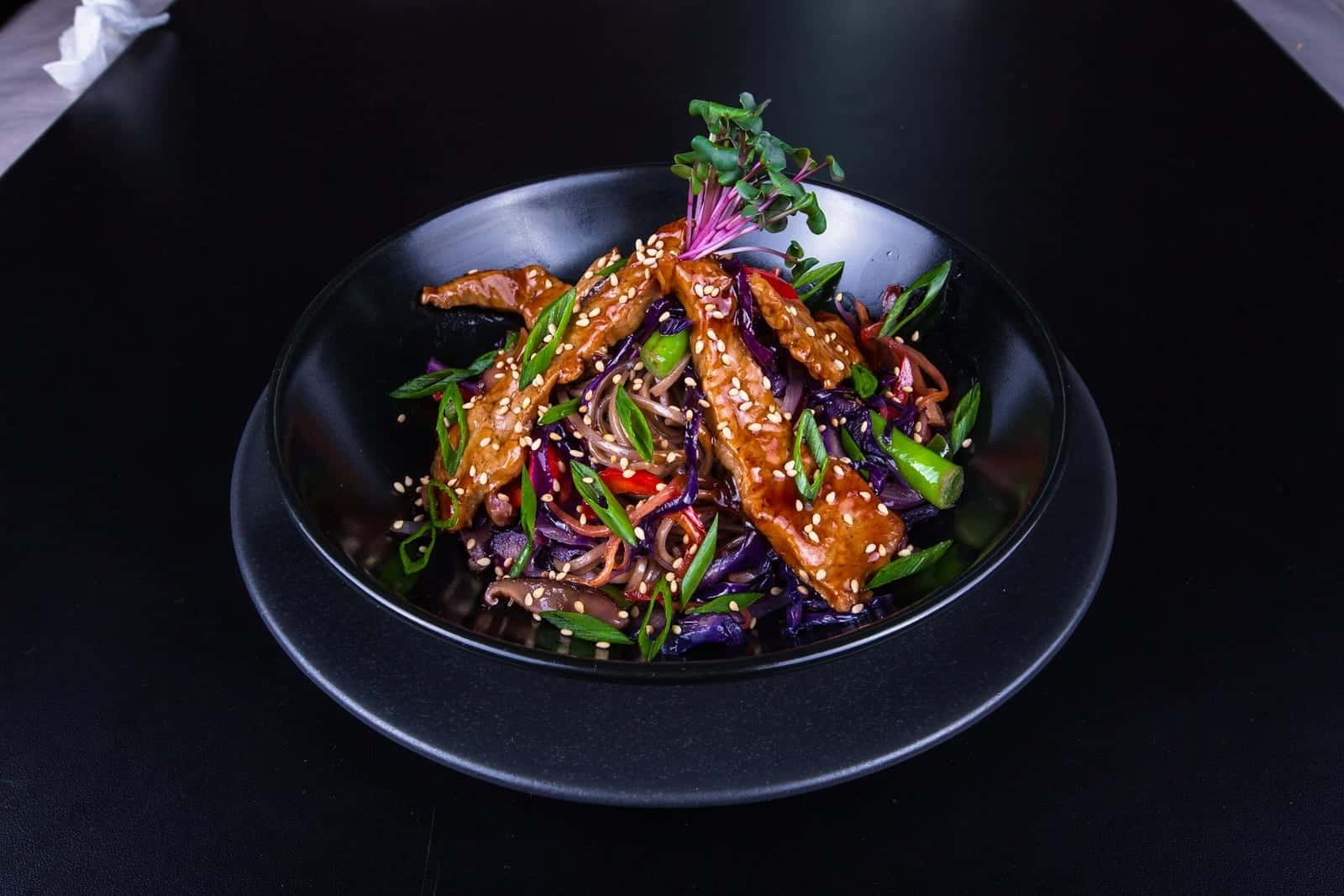 Sesame ginger chicken stir-fry with vegetables and noodles in a black bowl