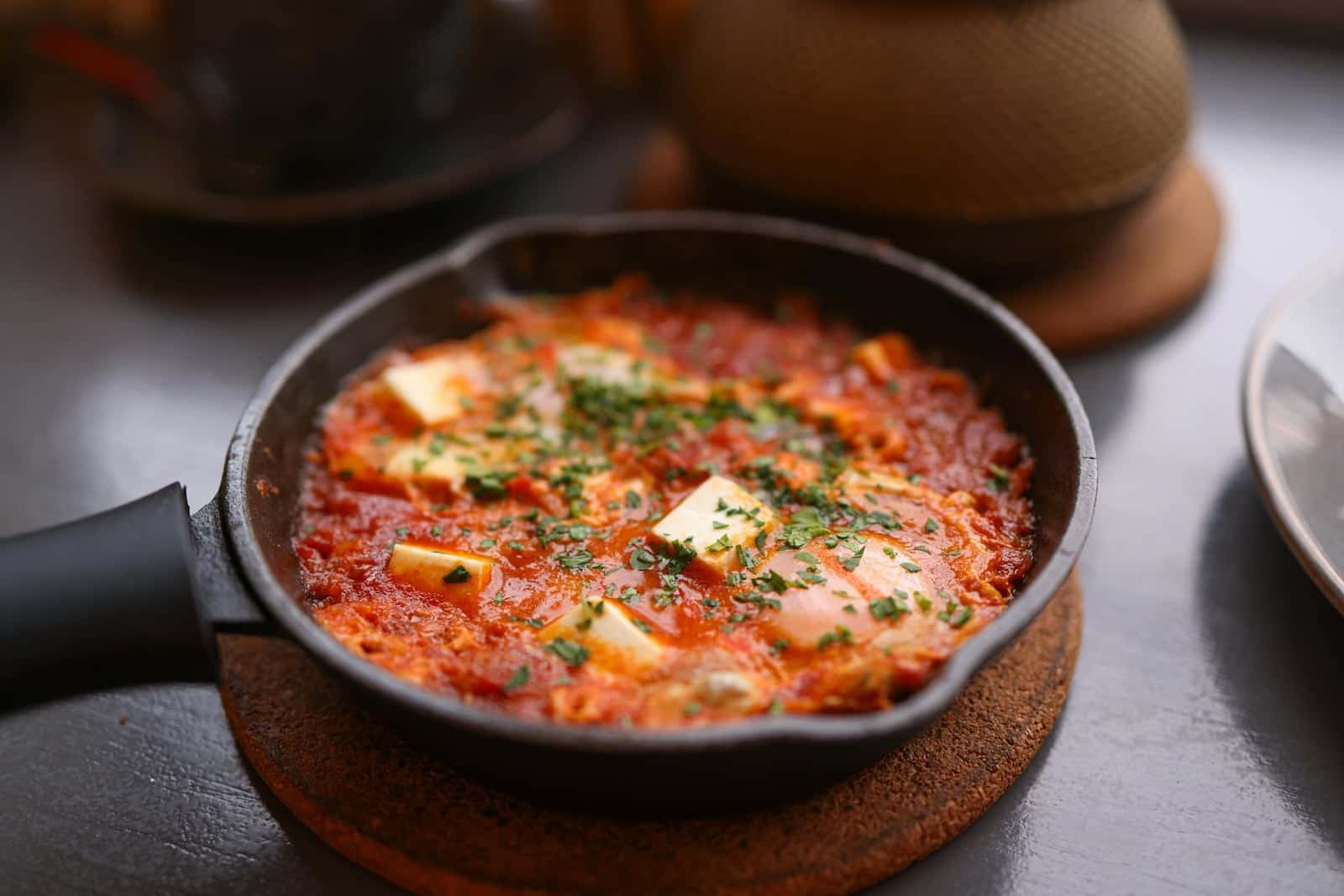 Shakshuka with feta in a skillet with poached eggs, tomato sauce, and fresh herbs
