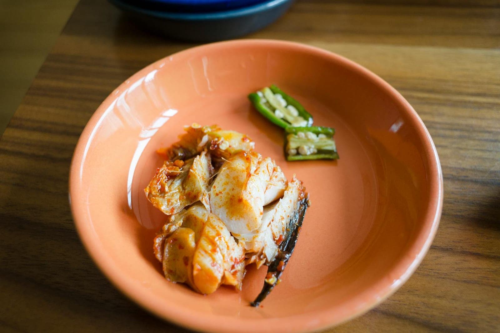 Singaporean chili crab pieces in a bright orange bowl with green chili and glossy sauce