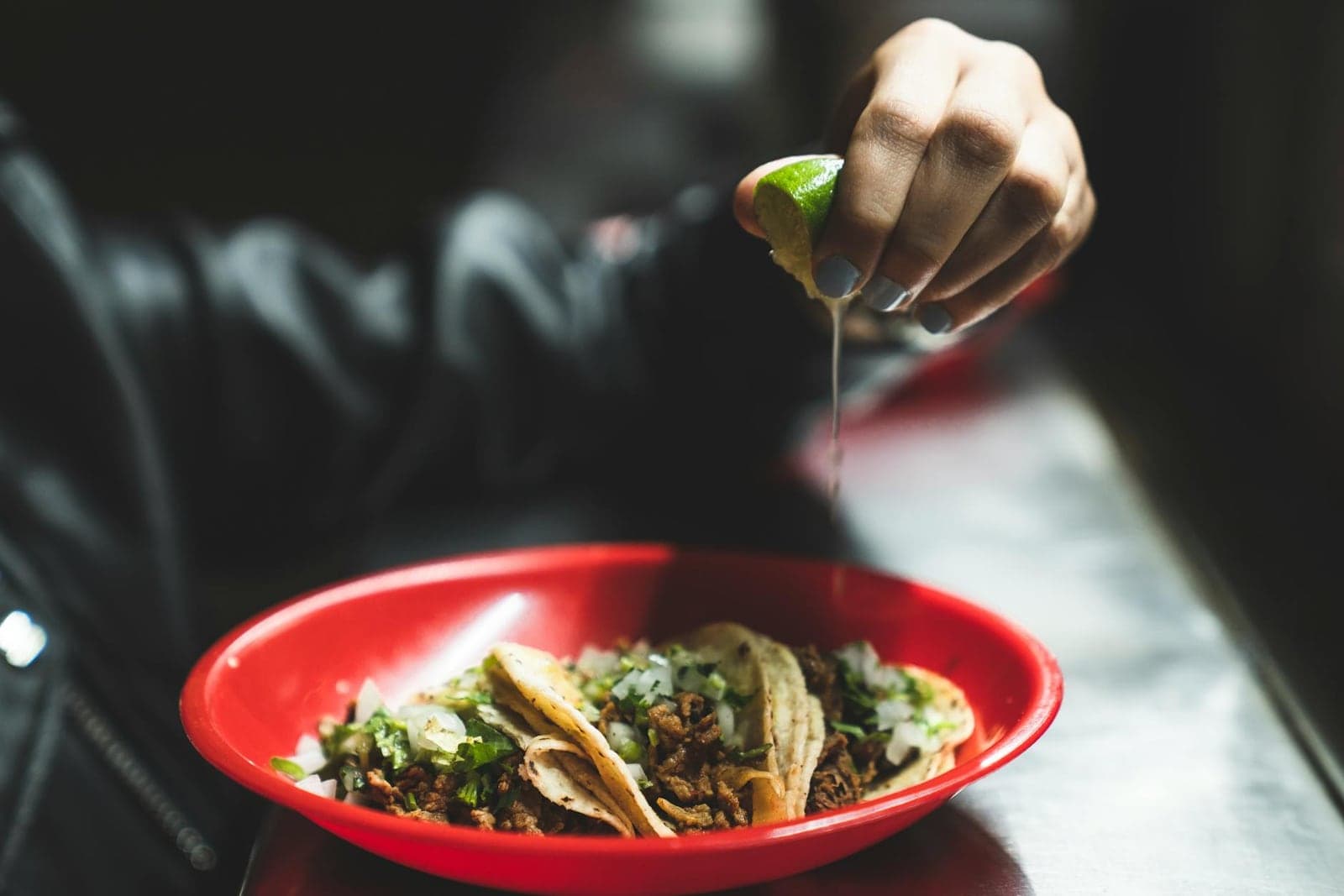 Slow-cooker carnitas tacos in a red bowl with lime squeezed over pork and herbs