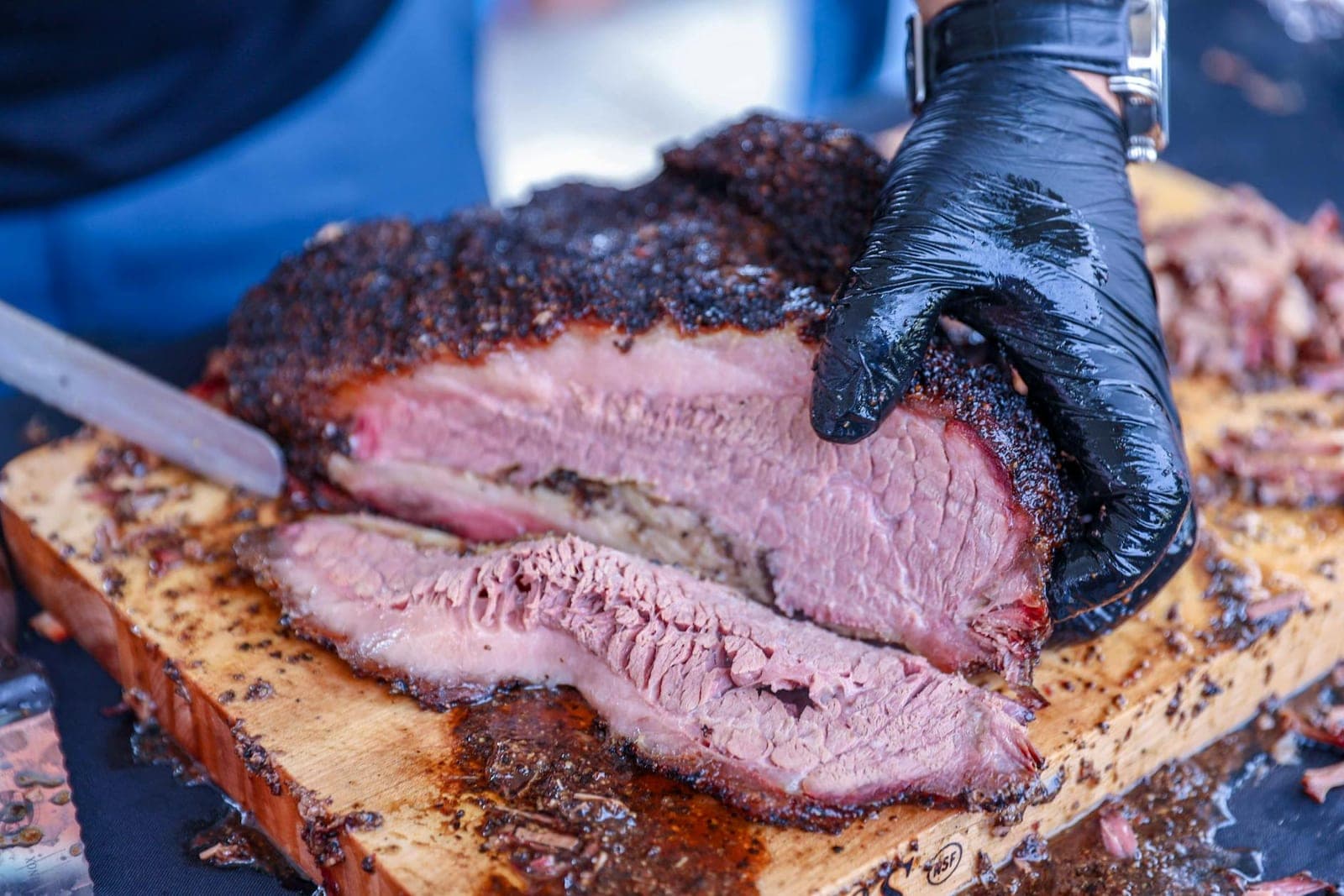 Sliced smoked-style beef brisket with a dark bark on a wooden cutting board