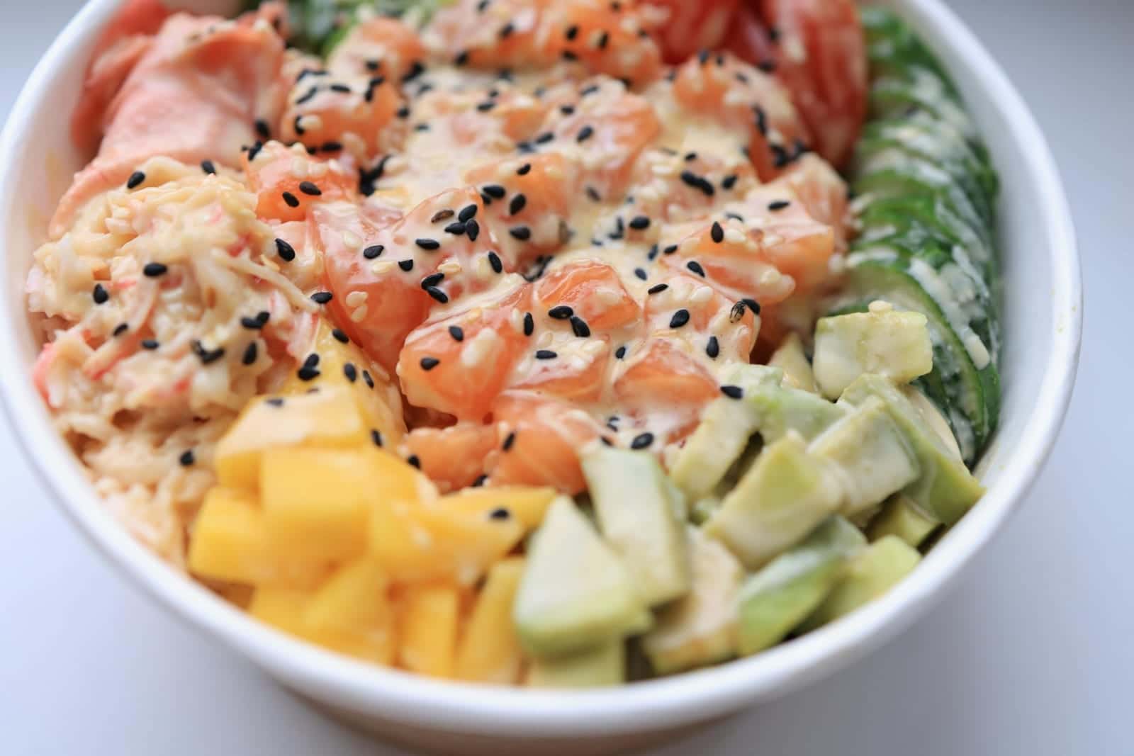 Spicy salmon poke bowl with avocado, mango, rice, sesame, and creamy sauce