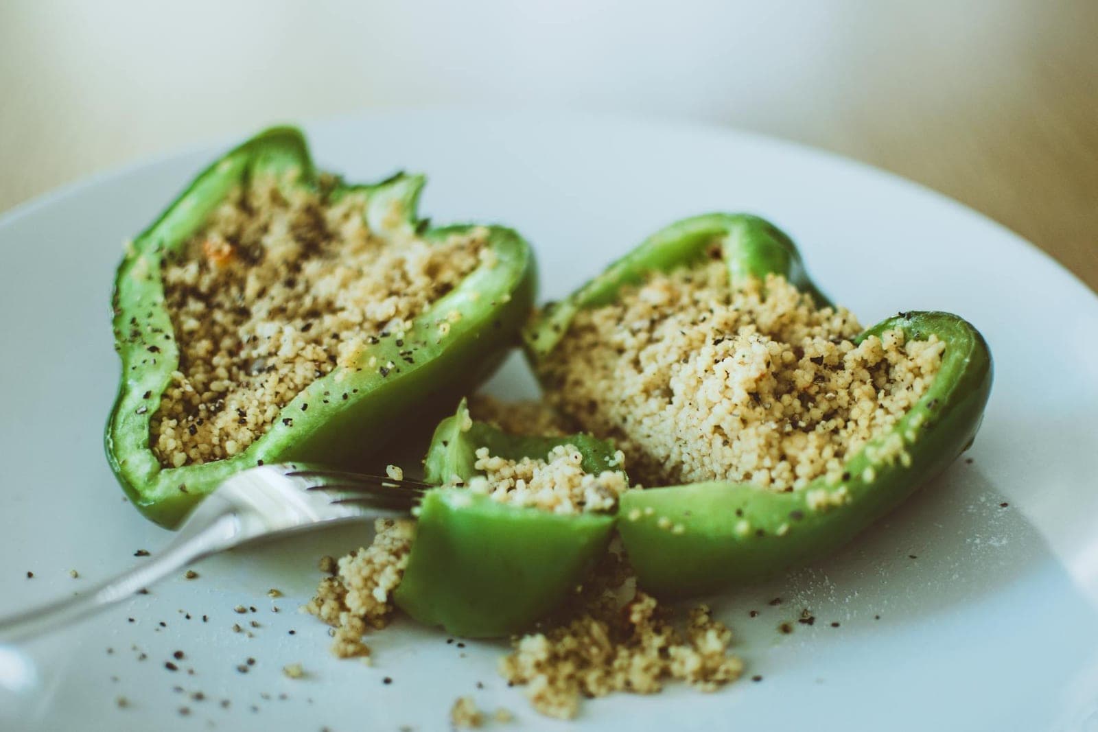 Stuffed grilled green bell peppers filled with couscous on a white plate
