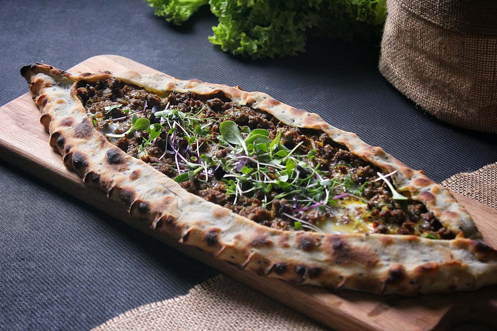 Turkish pide with minced meat filling and herbs on a wooden board