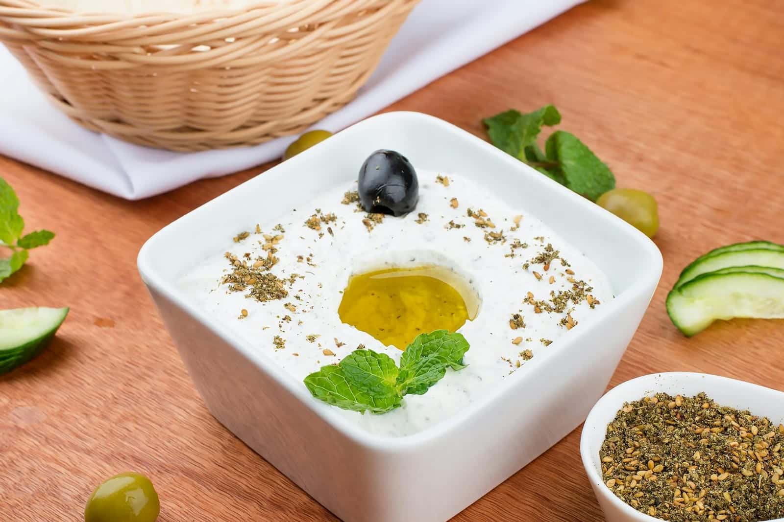 Tzatziki sauce in a white bowl with olive oil, mint, cucumber, and dried herbs