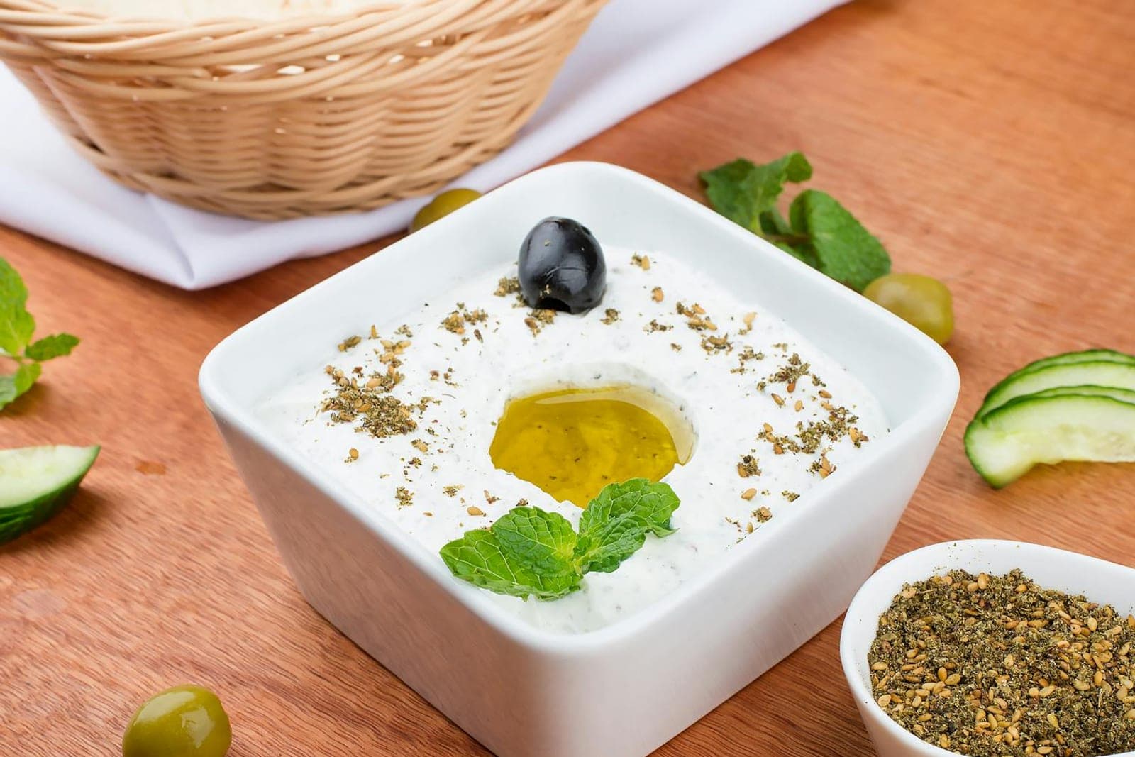 Tzatziki sauce in a white bowl with olive oil, mint, cucumber, and dried herbs