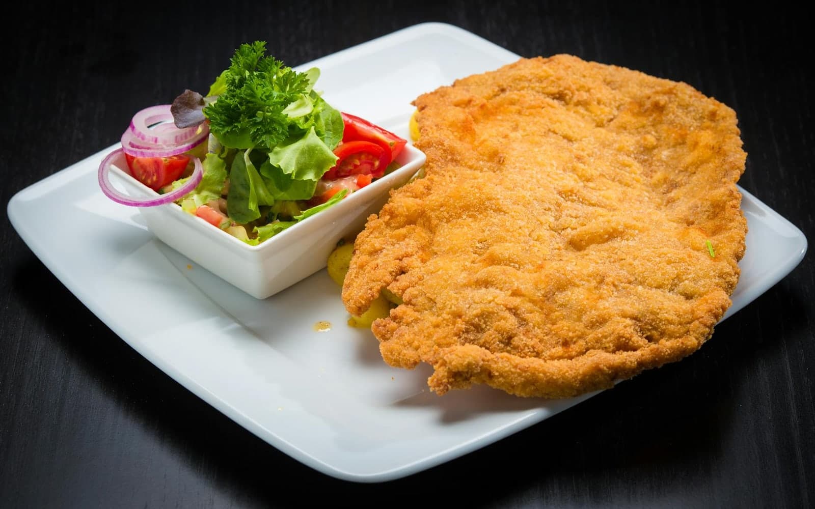 Veal piccata cutlet with a golden crust, salad, and lemon on a white plate
