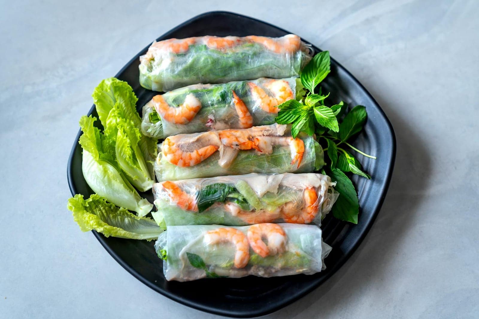 Vietnamese fresh spring rolls with shrimp, lettuce, herbs, and rice paper on a black plate