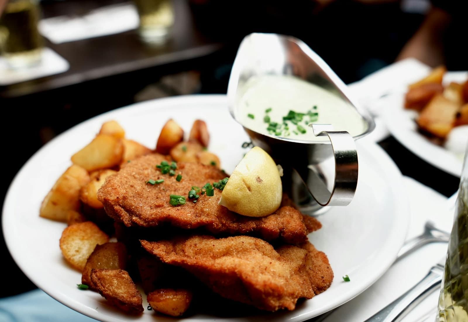 Wiener schnitzel with lemon, roasted potatoes, and creamy sauce on a restaurant plate
