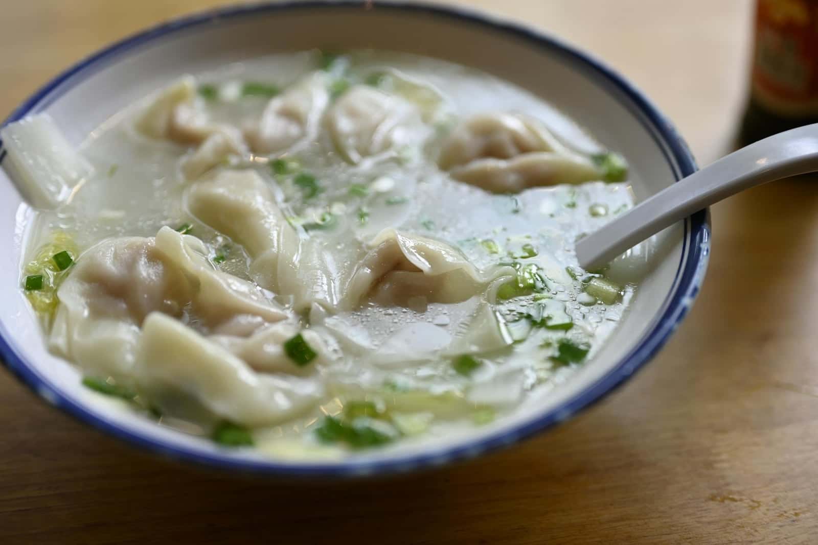 Wonton soup in a blue-rimmed bowl with dumplings, clear broth, and scallions