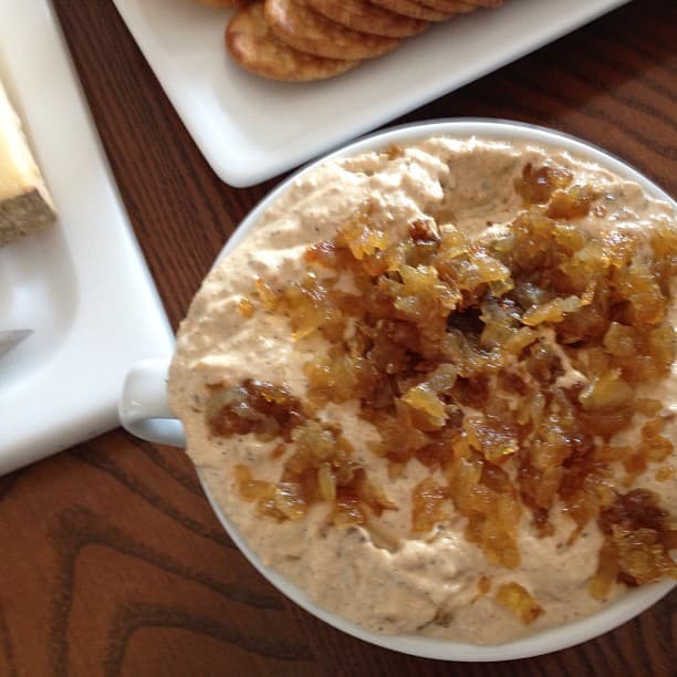 Bowl of French onion dip with caramelized onion swirled through, surrounded by potato chips